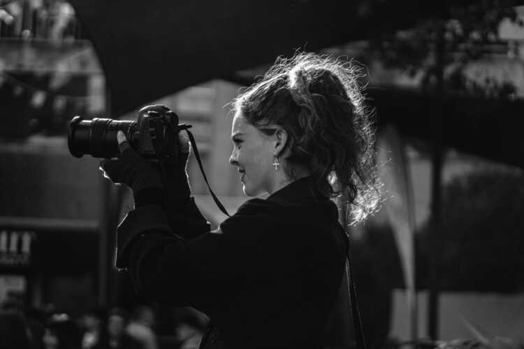grayscale photo of woman in black jacket holding dslr camera
