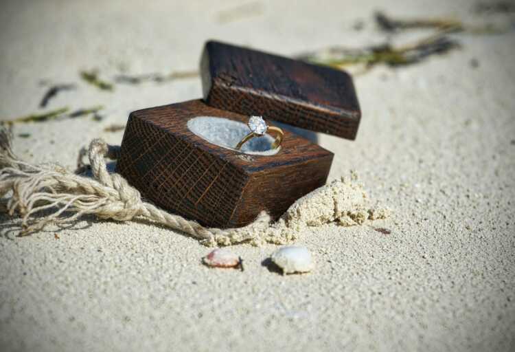 gold-colored clear gemstone ring in brown wooden box on sand