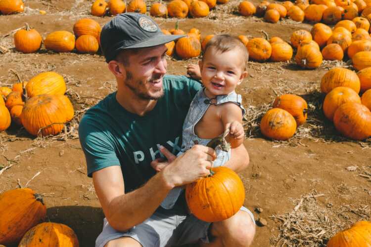 smiling man carrying toddler boy while holding pumpkins